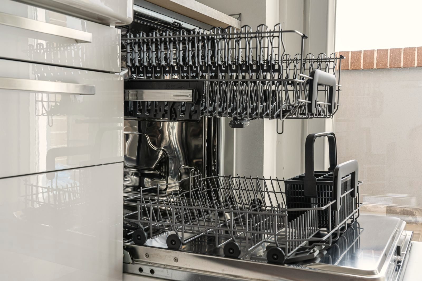 The open, empty rack of a stainless dishwasher