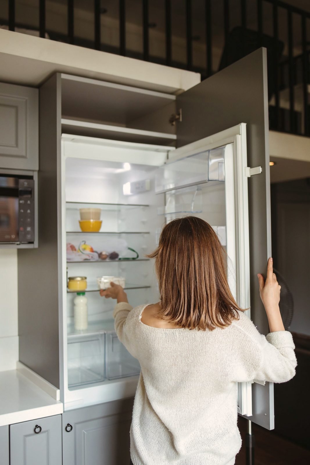 A person standing at an open refrigerator in a kitchen