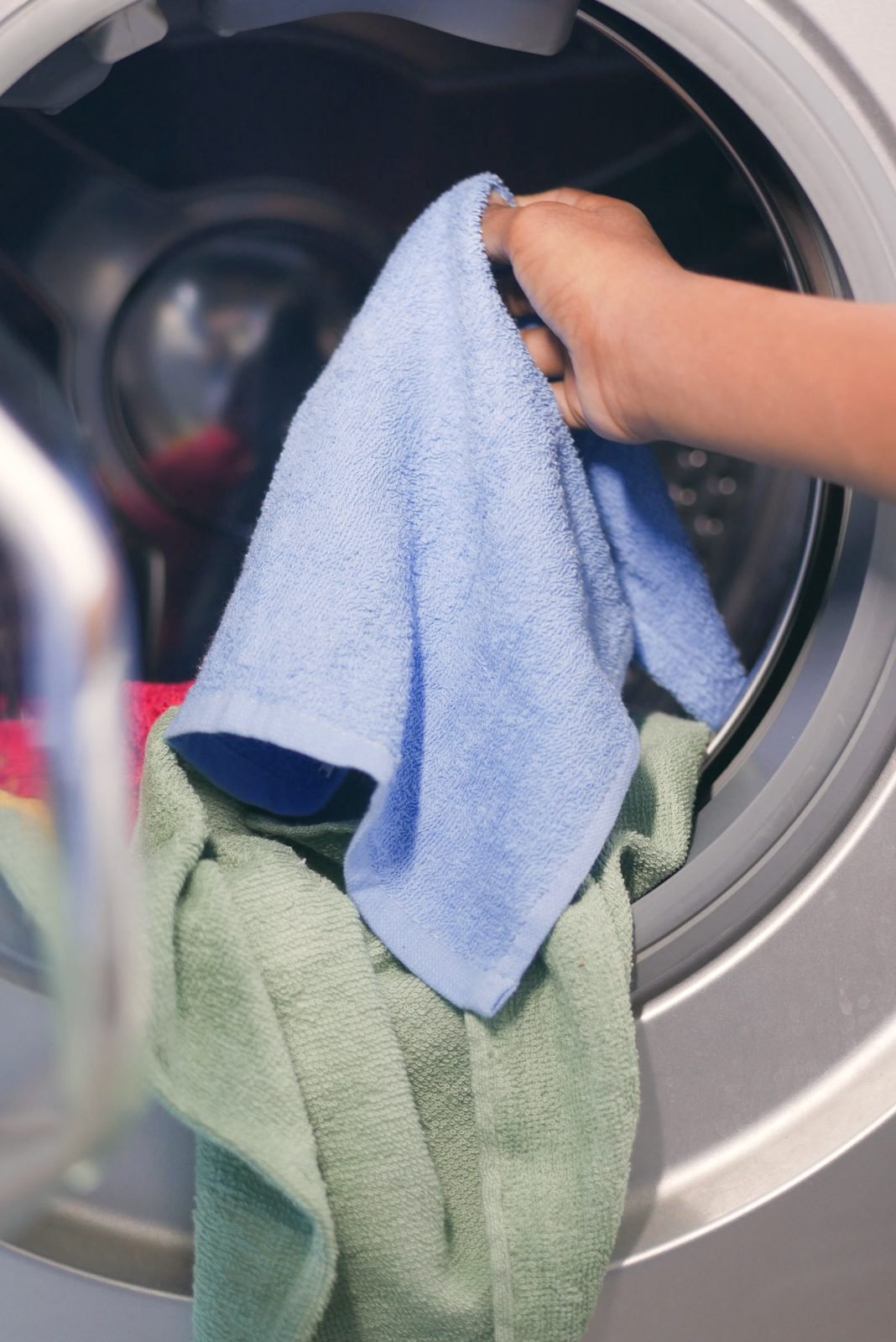A hand loading a towel into a front-load washer